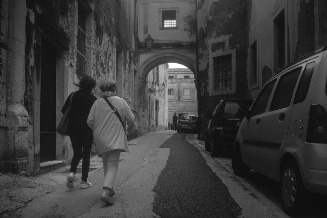 Black-and-white view of pedestrians walking through an old Italian street